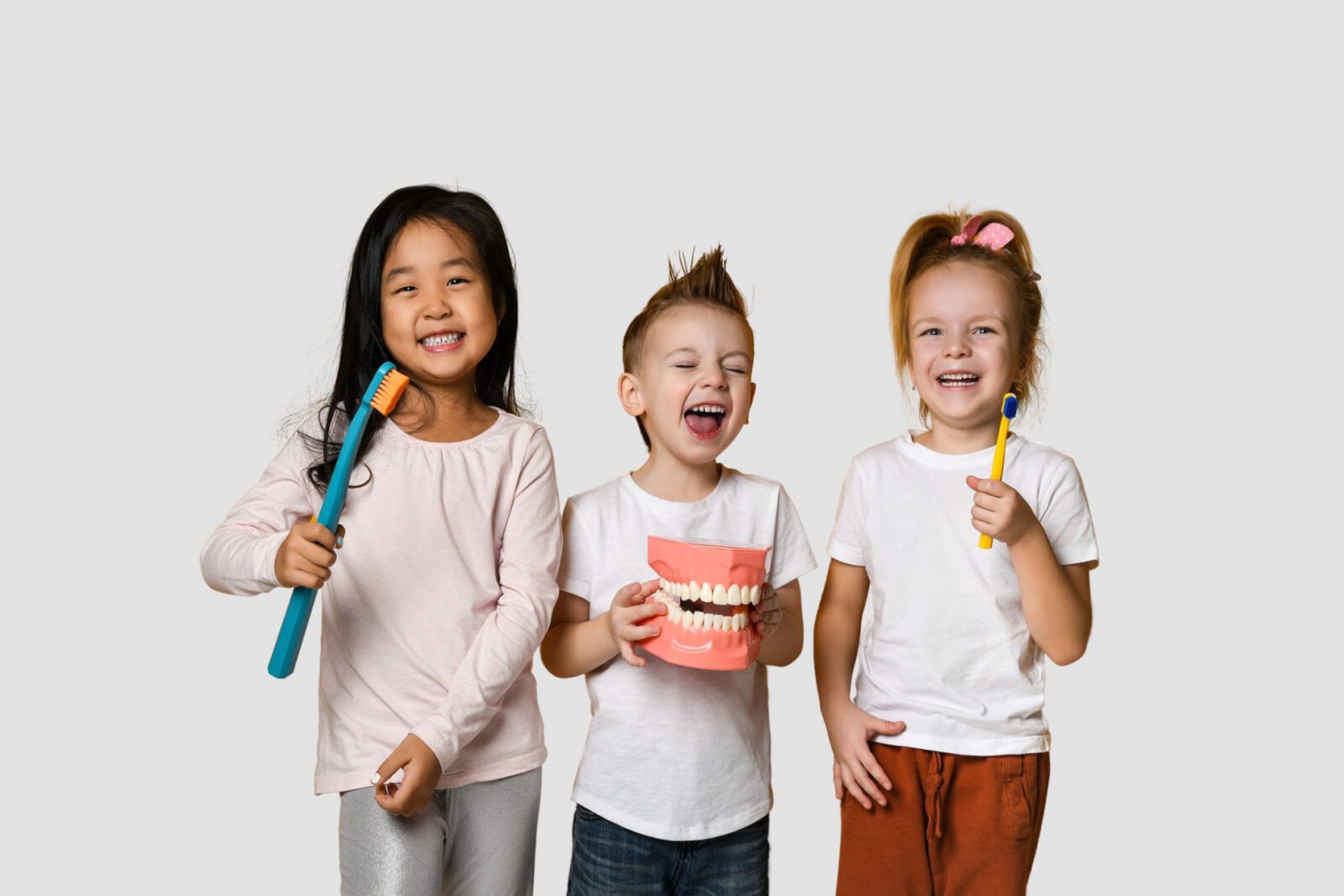 Three children are standing together holding toothbrushes and a model of teeth.