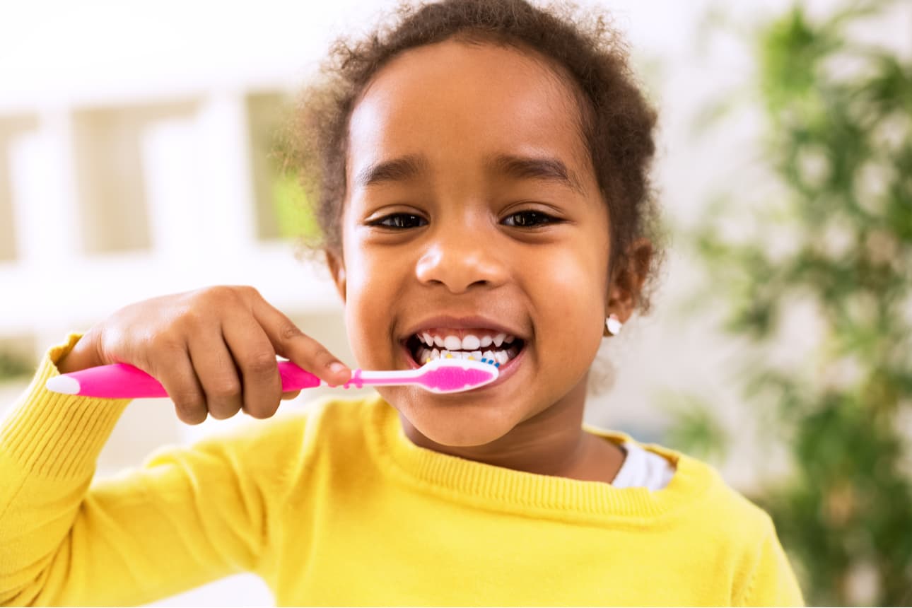 A young child is brushing her teeth with a pink toothbrush.